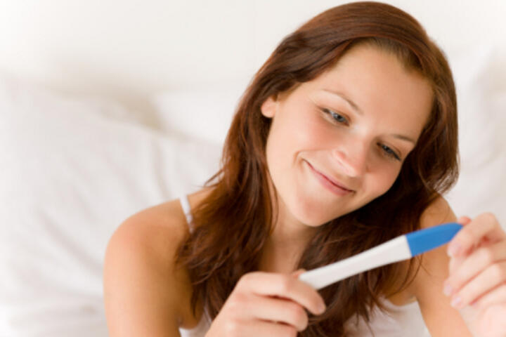 Immagine di donna sorridente che guarda un test di gravidanza positivo
