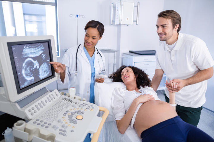Immagine di una ginecologa che esegue l'ecografia morfologica, mentre il futuro papà tiene la mano alla futura mamma