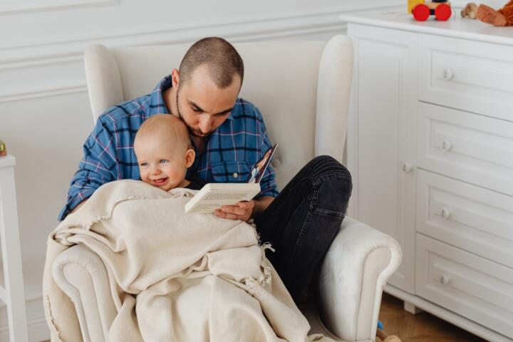 Neopapà legge un libro con il braccio un neonato
