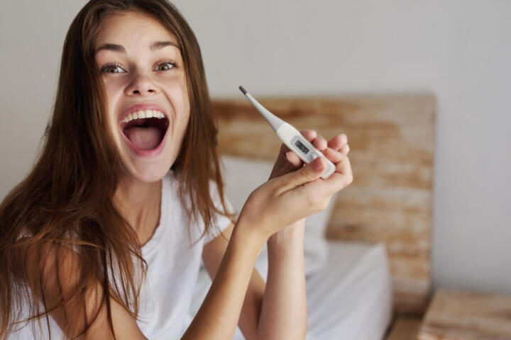 Immagine di donna felice con termometro in mano: molte donne riferiscono di aver provato una sensazione di febbre come sintomo di gravidanza.