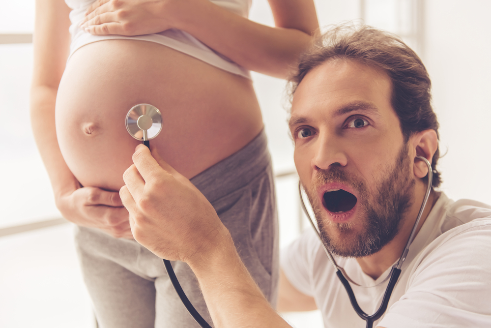 Un futuro papà ascolta il battito del bambino con uno stetoscopio sul pancione della compagna